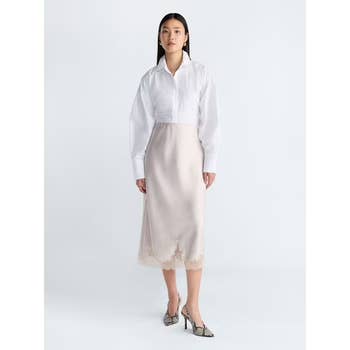 Woman in a sleek white blouse and elegant midi skirt with lace hem, wearing stylish pointed heels