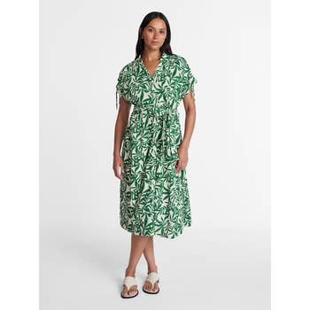 Person wearing a patterned midi dress with a belted waist and short sleeves, standing in a neutral setting