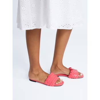 Person wearing coral slide sandals with scalloped details, paired with a white eyelet skirt