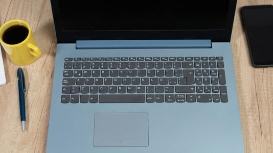 A laptop with a numpad sitting on a wooden table, with a phone, a cup of coffee, and a pen nearby