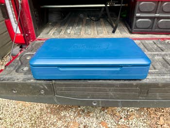 A closed blue Coleman camping stove case sits on the tailgate of a truck