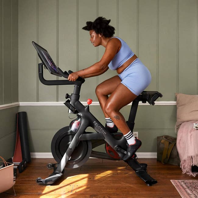 Person in athletic wear using a Peloton bike at home, focused on the screen