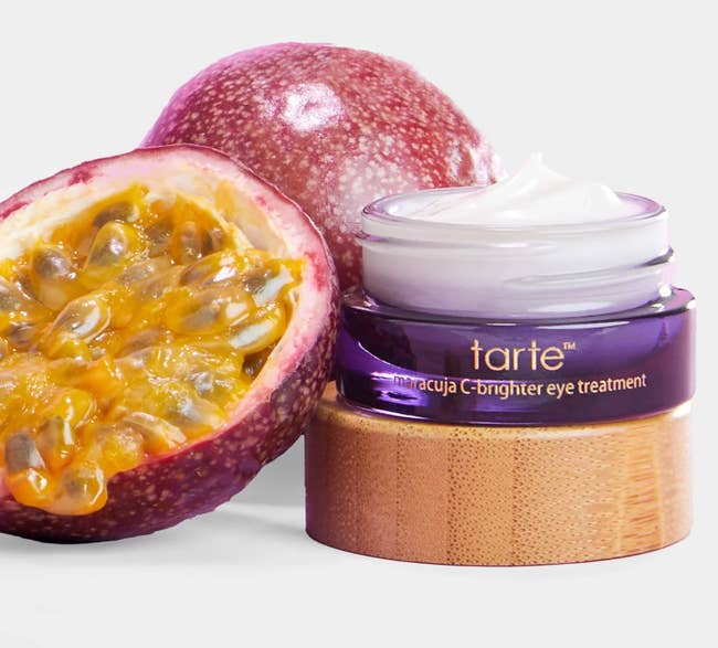 Tarte Maracuja C-Brighter Eye Treatment jar sits beside a cut-open passion fruit, highlighting natural ingredients for skincare