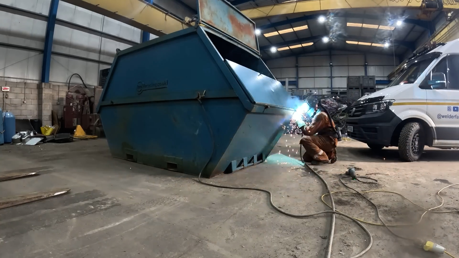 Welder repairing industrial skip container during heavy-duty steel ...