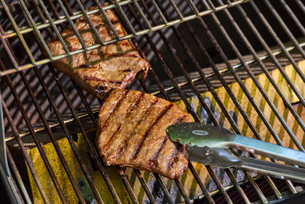 Tongs flipping a steak being cooked on the Weber Searwood 600 Pellet Grill