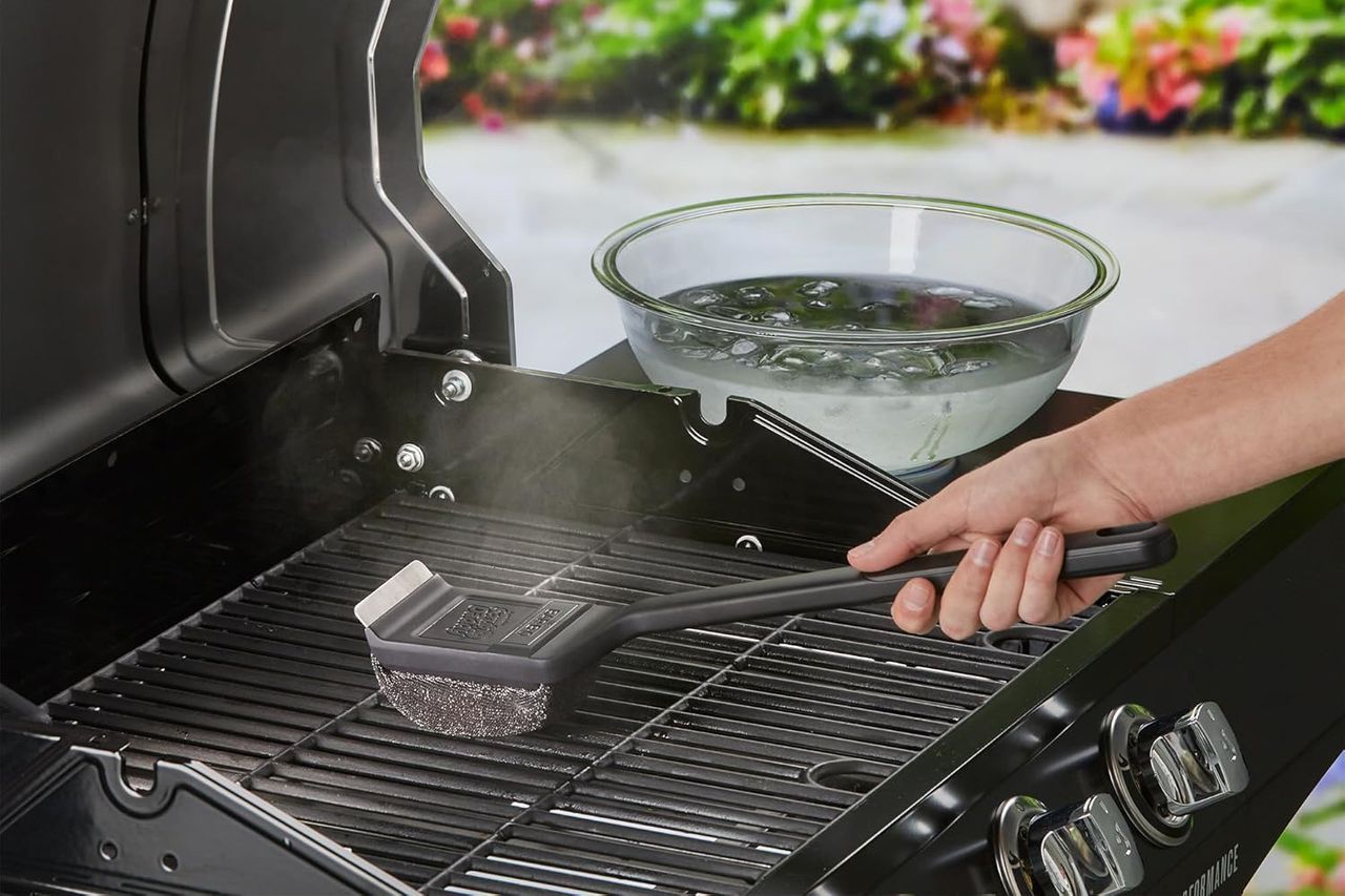 A person cleaning a barbecue grill grate using a steam brush a bowl of water nearby