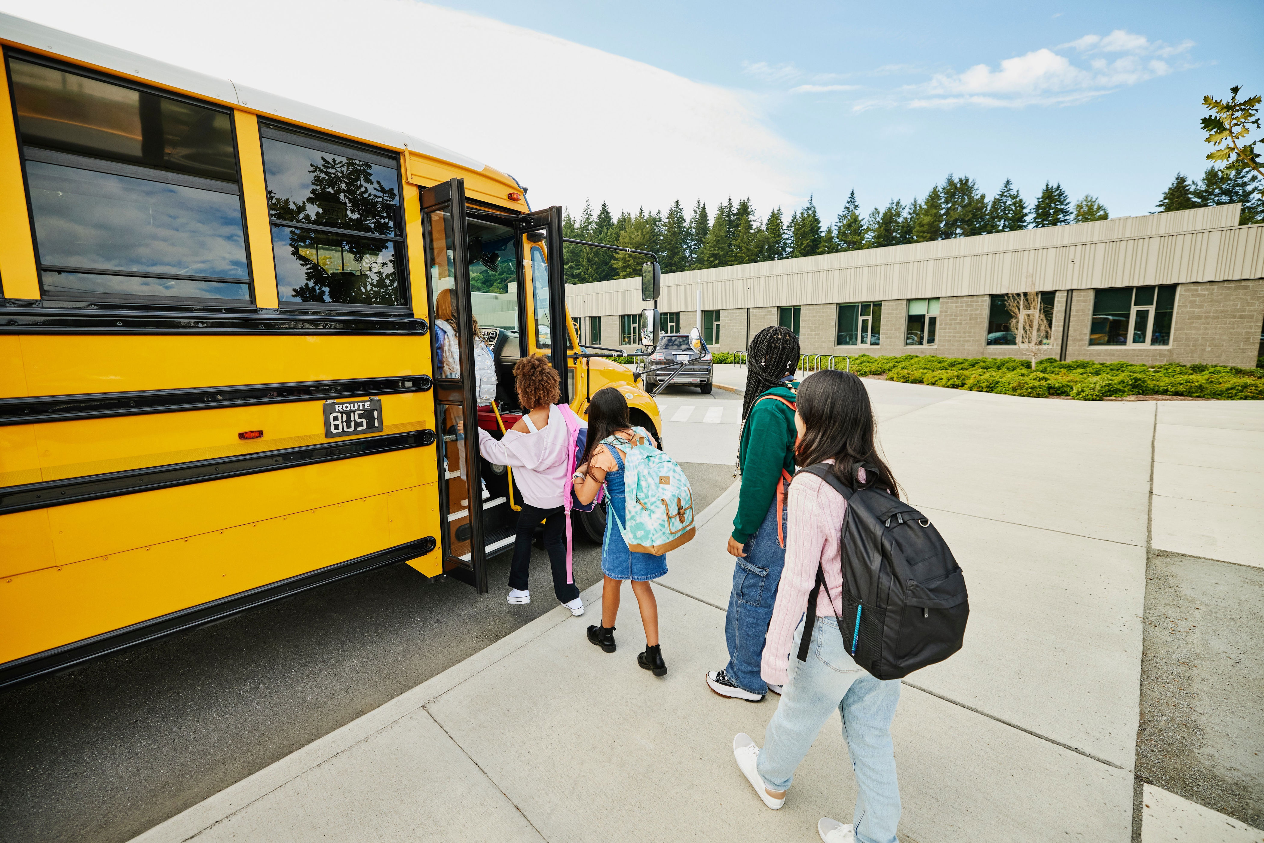Children with backpacks boarding a school bus outside a school building