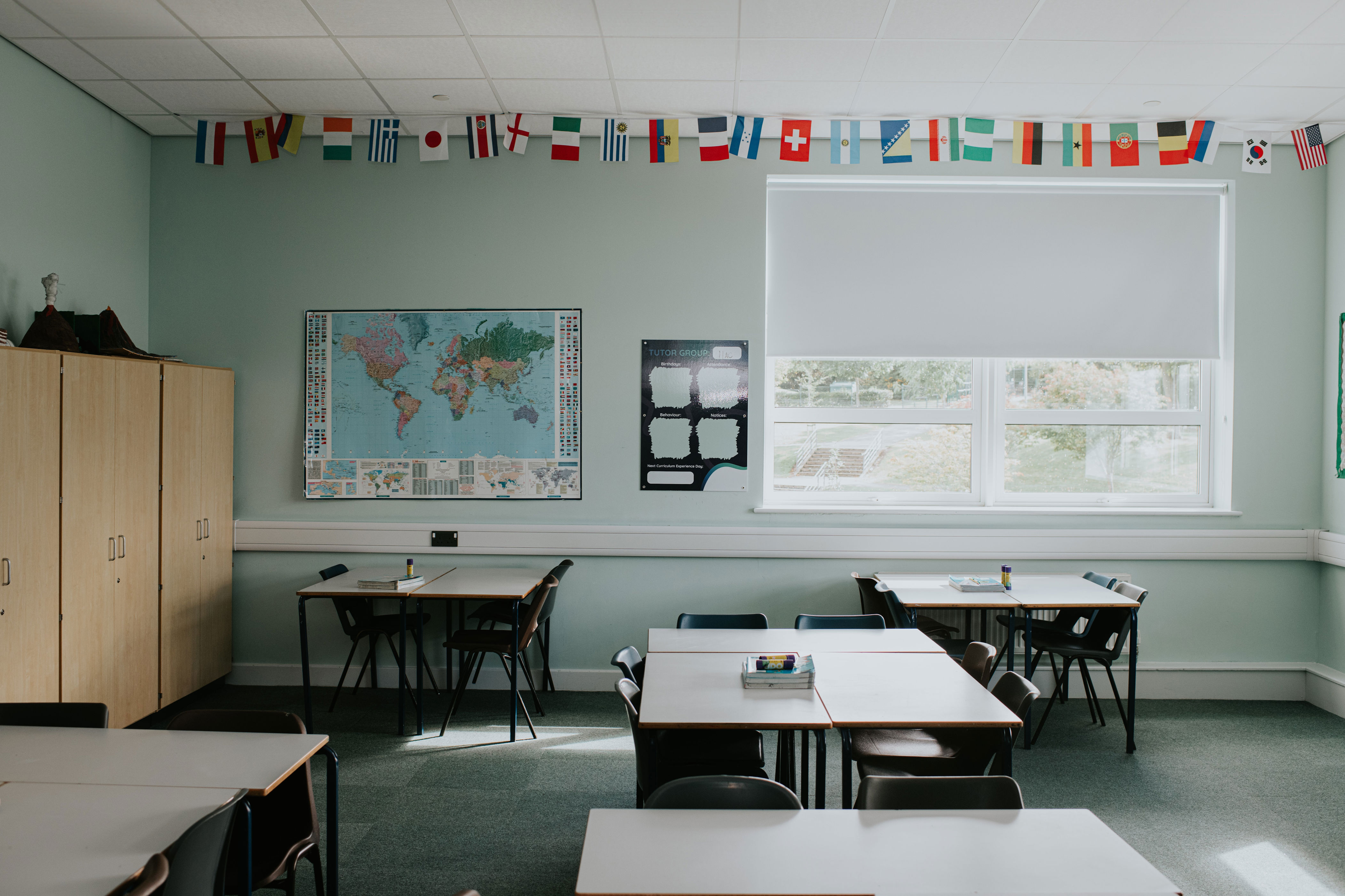 Classroom with international flags, world map, and multiple desks. Bright, organized space with ample natural light from a window