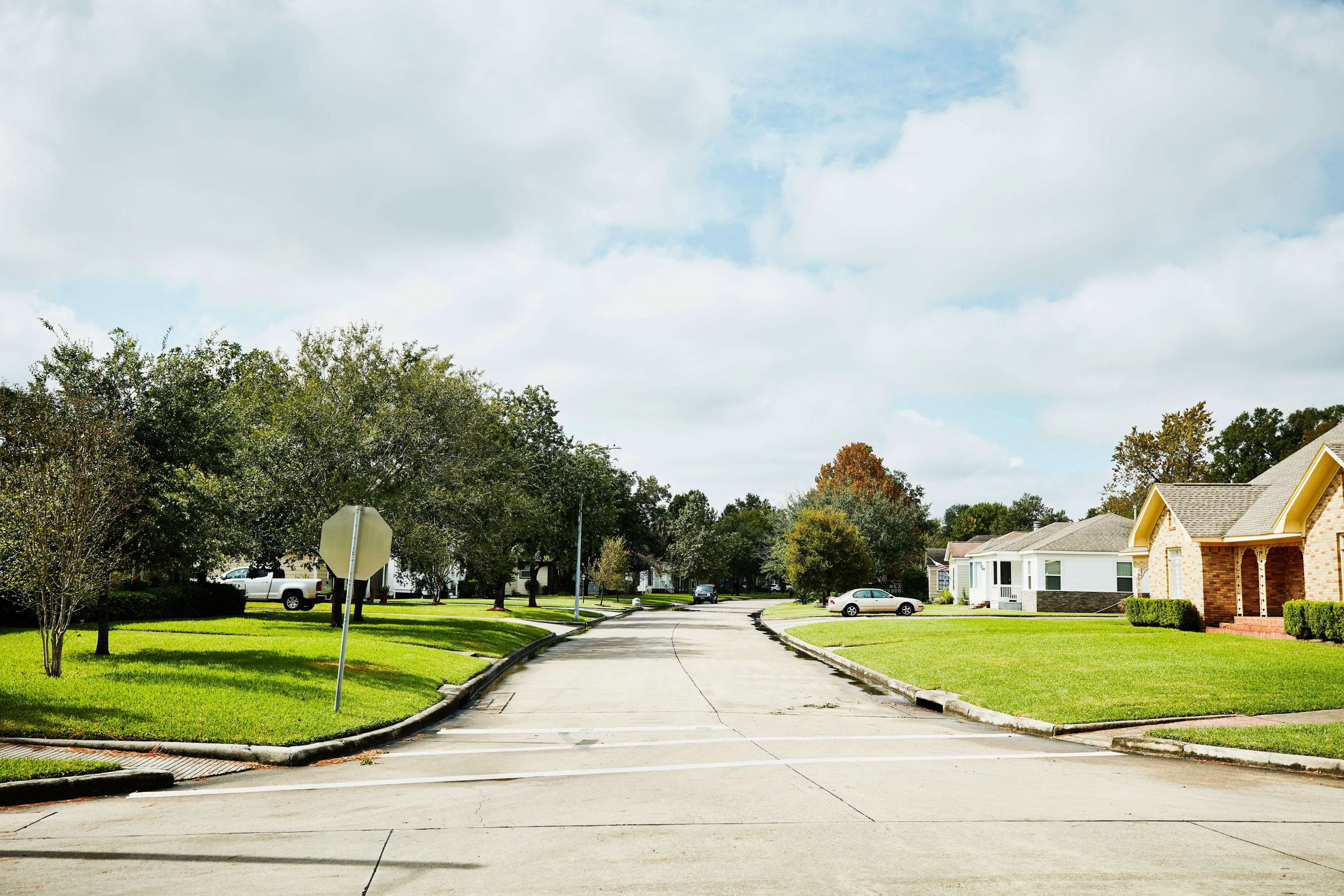 A quiet suburban street with houses, trees, and a stop sign, under a cloudy sky