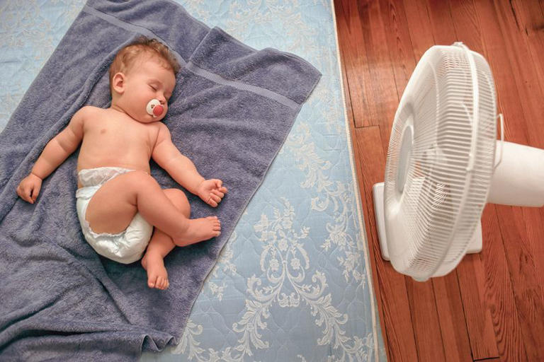Baby sleeping on mattress with electric fan to beat extreme summer heat