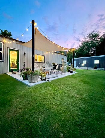 Cozy backyard patio with string lights, a sail canopy, wicker furniture, and potted plants at dusk