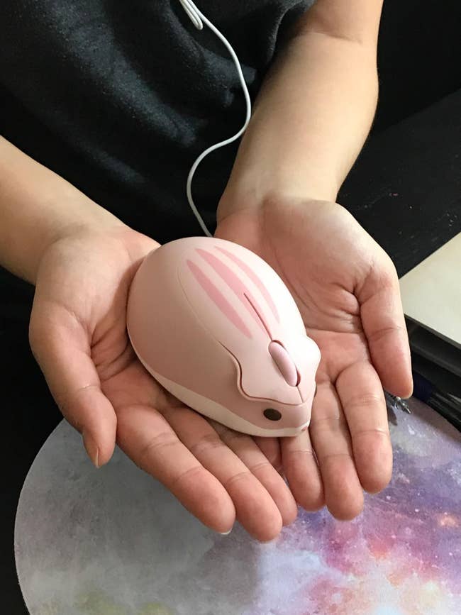 Person holding a mouse-shaped computer mouse in their hands over a cosmic-patterned mouse pad