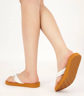 Person's legs wearing slip-on sandals with thick soles, walking on a plain surface