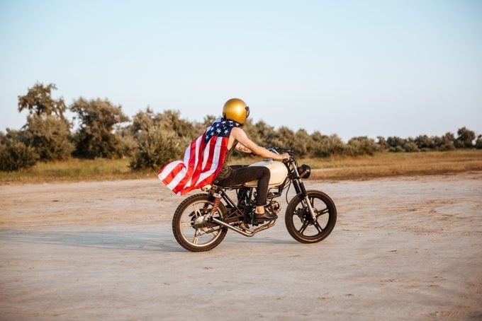 Side View Of Man In American Flag Cape Driving Motorcycle