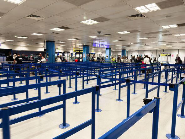 Busy Manchester Airport border control queues with blue barriers and travelers waiting