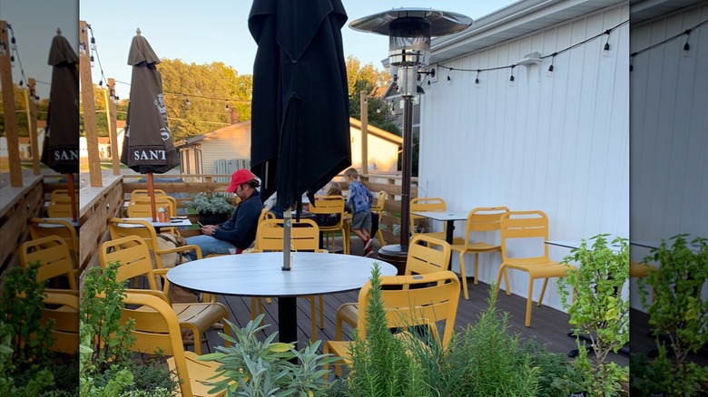 Customers sit on outdoor patio at pizzeria and market Branch and Daughter, with tables, yellow chairs, and plants