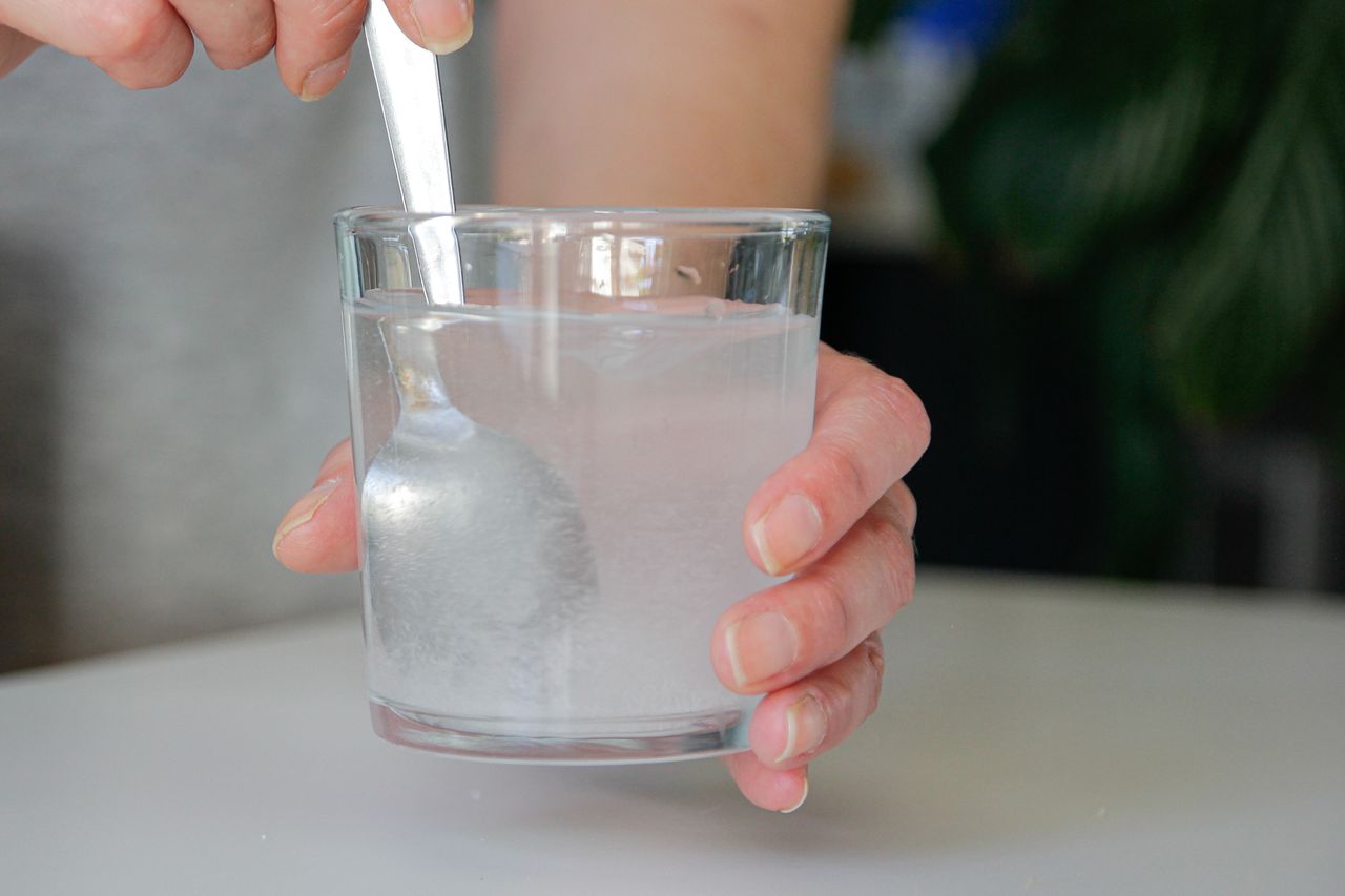 A person stirring a glass of liquid with a spoon