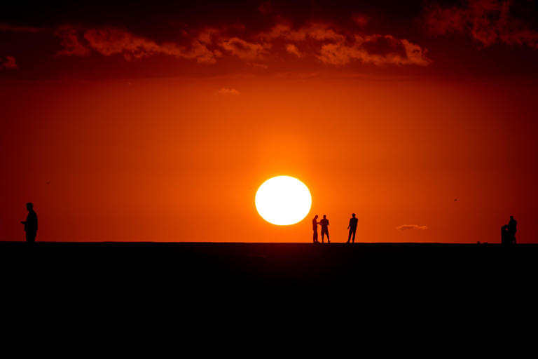 silhouettes of people in front of an orange sunset over the ocean 