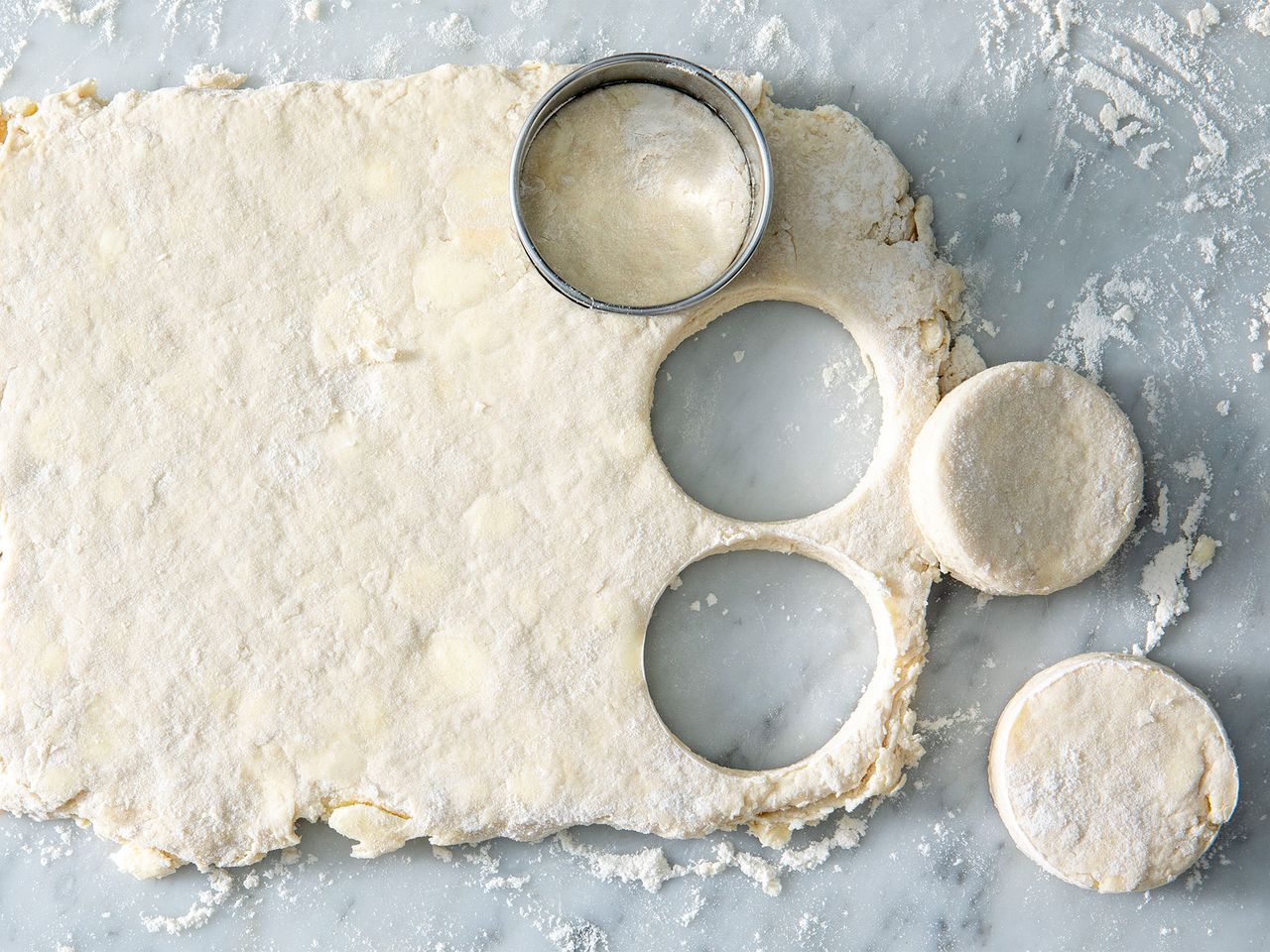 Dough rolled out with round biscuit shapes cut out using a cutter resting on a floured surface