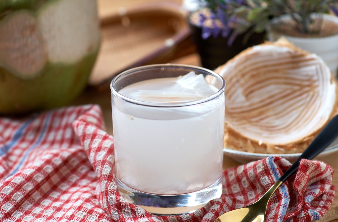 A glass of a clear beverage with ice a dessert plate and a red checkered cloth
