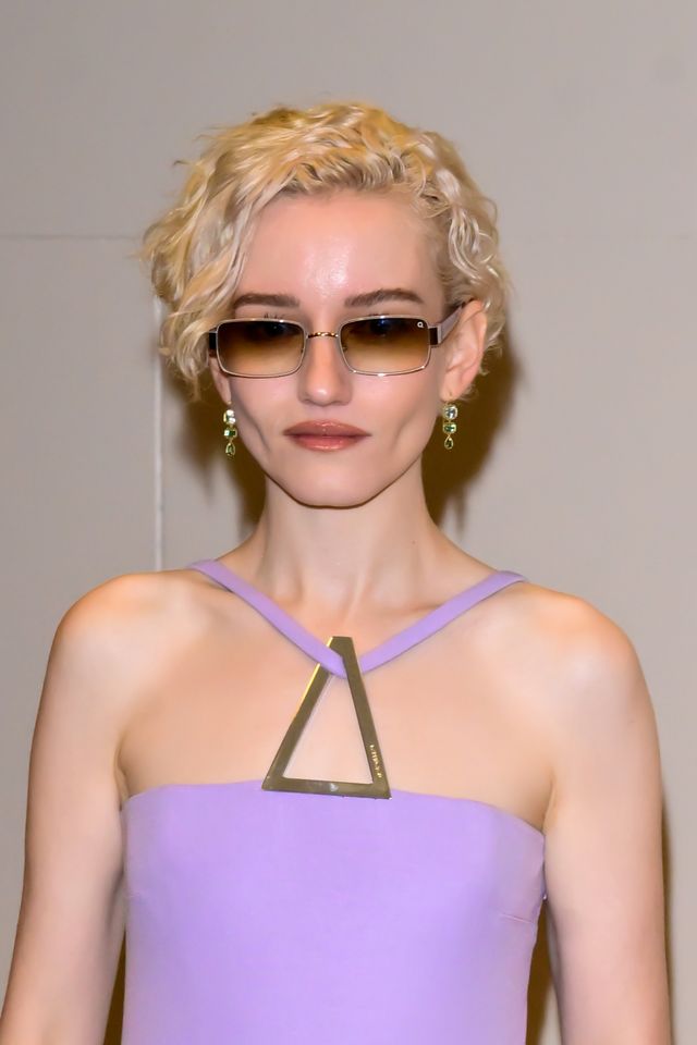Julia Garner wearing sunglasses and a light purple outfit looking at the camera