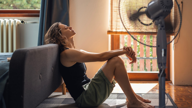 Young woman suffering from heat sitting at home on the floor in front of a fan