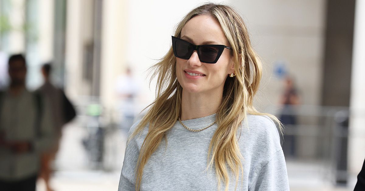 Olivia Wilde wearing a gray sweatshirt, satin knee-length skirt, and ruched loafers in London