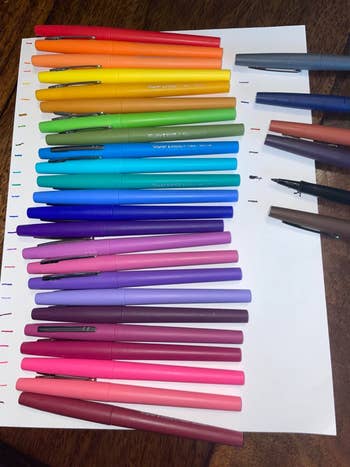 An array of colorful pens laid out on a piece of paper, each showing ink color through small drawn lines next to them