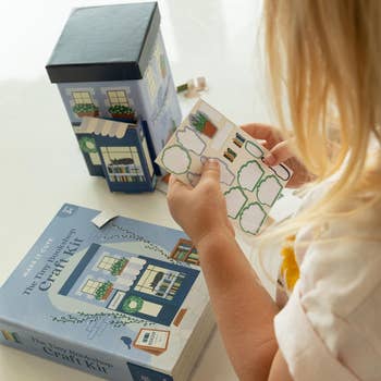 A child assembling a miniature bookshop craft kit, includes a model house and stickers