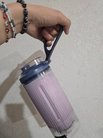 Person holding a portable blender filled with a purple smoothie, demonstrating ease of use