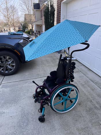 Wheelchair with stylish geometric-patterned umbrella attached, parked in a driveway near a house