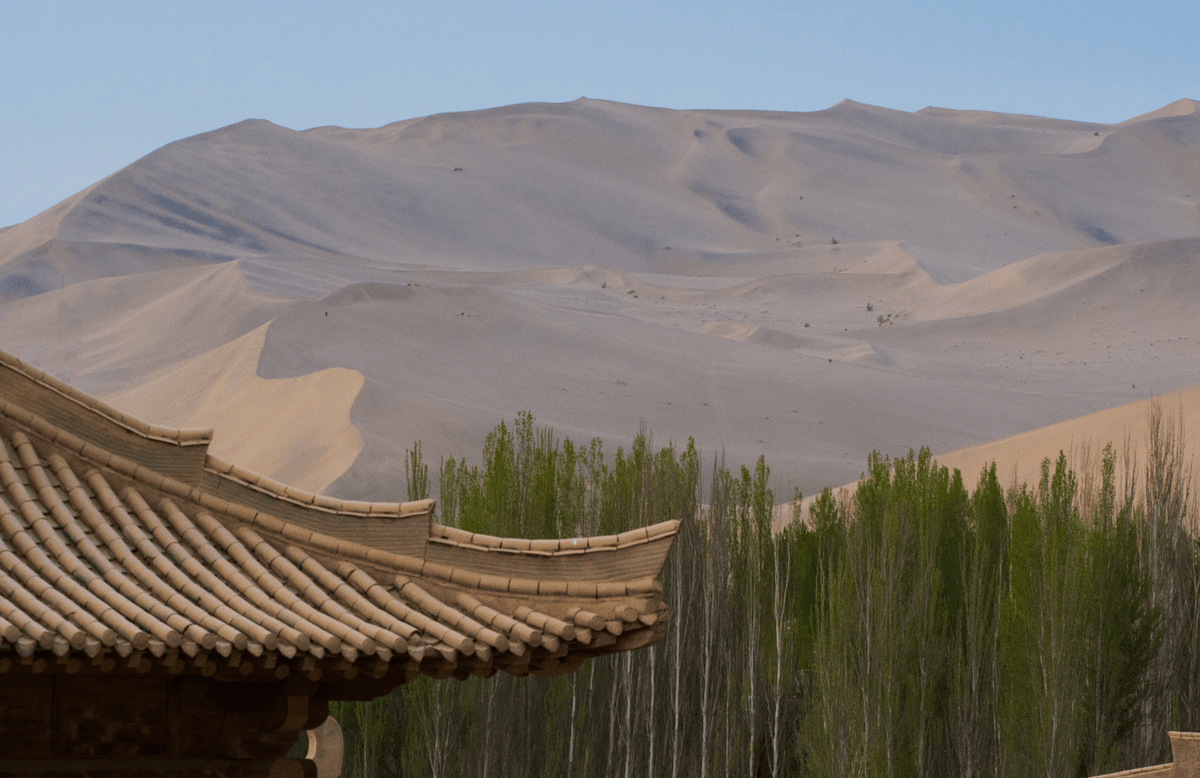 The Mingsha Desert peeks over an old-style house and fresh forests in Gansu Province, Northwestern China. - Image credit: Bonn_A/Shutterstock.com