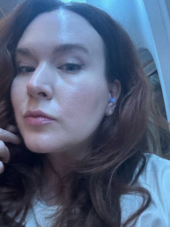 Woman with long, wavy hair using wireless earbuds, posing indoors