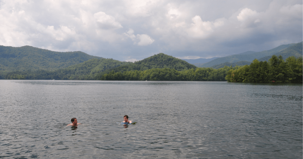 Two swimmers at Santeelah Lake in North Carolina, with mountains surrounding and cloudy sky overhead.