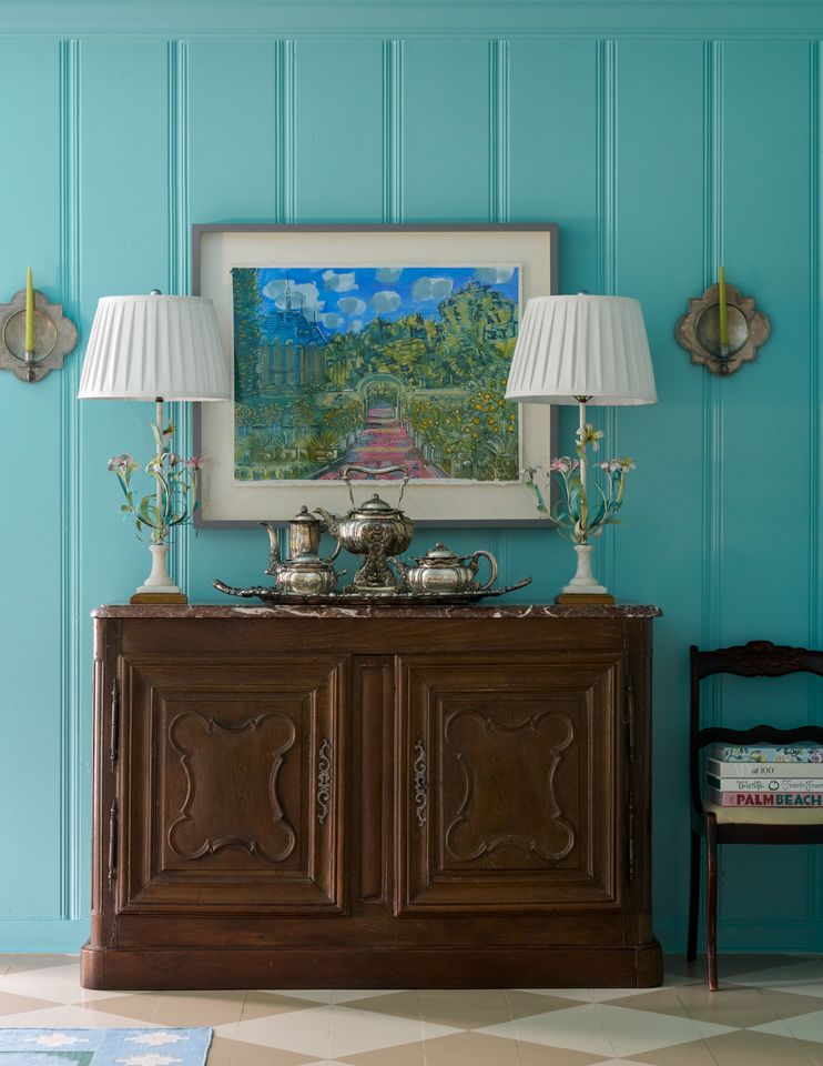 A wooden cabinet with ornate designs flanked by two table lamps set against a blue paneled wall