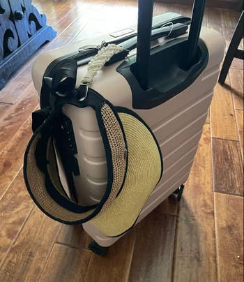 A suitcase with a hat and a purse attached to its handle sits on a wooden floor