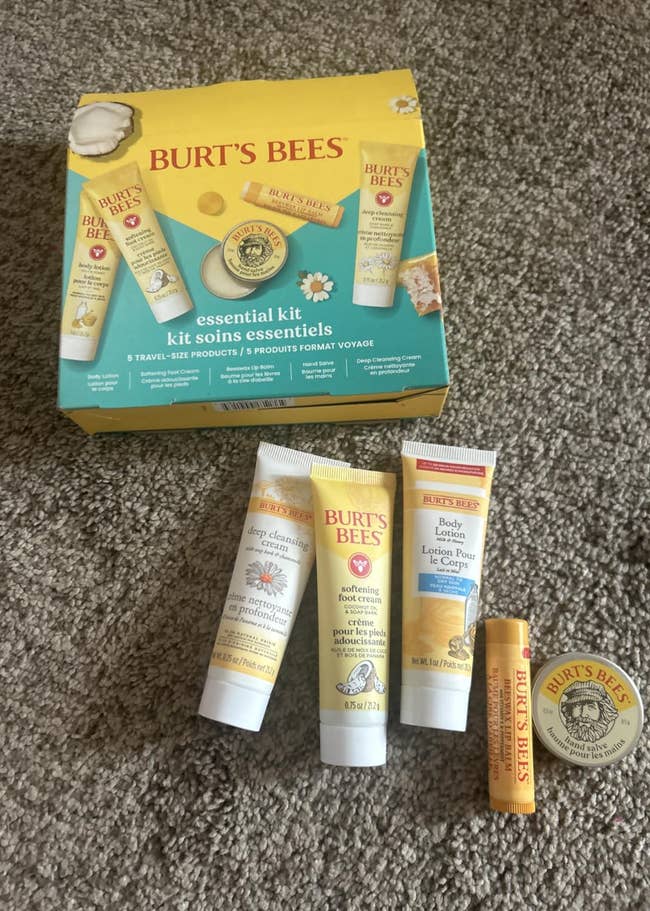 Burt's Bees Essential Kit with travel-size skincare products displayed on a carpet, including creams and lip balm, alongside box packaging