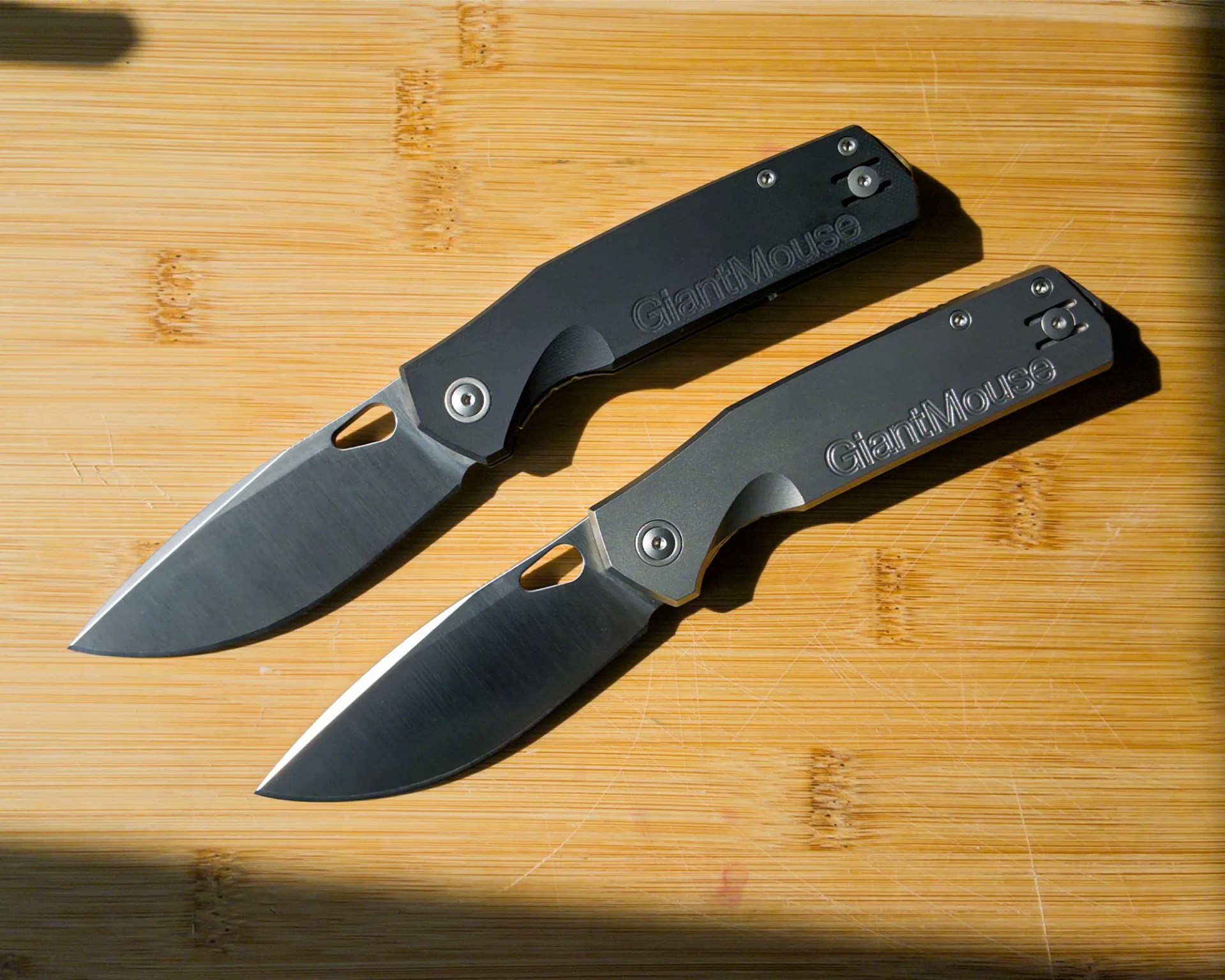 Two black-handled folding knives with partially visible blades on a wooden surface.