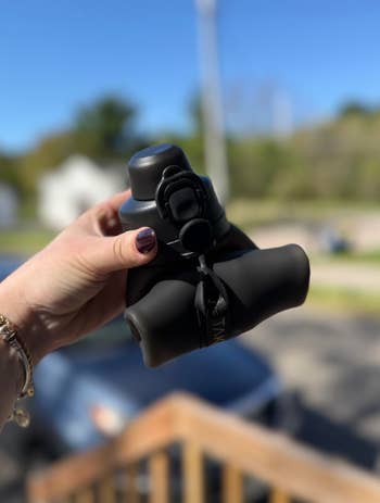 Person holding a collapsible, silicone travel mug outdoors, suitable for on-the-go use