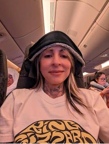 Person on an airplane wearing a casual graphic T-shirt and hooded jacket, seated among other passengers