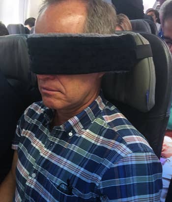 Person on plane wearing a large, padded sleep mask while sitting in an airplane seat
