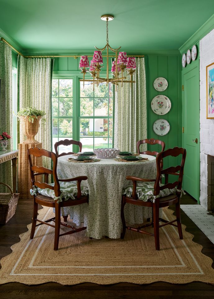 Dining room with a round table chairs and greenpainted walls featuring large windows and decorative plates