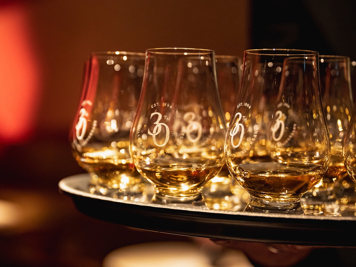 Sullivans Cove whisky glasses on a tray, each filled with amber liquid, warmly lit in a dim setting.