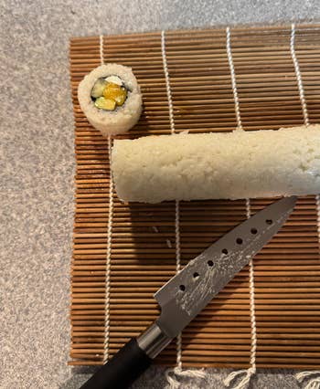 Sushi roll being sliced on a bamboo mat, revealing a piece with mango and avocado filling next to a knife