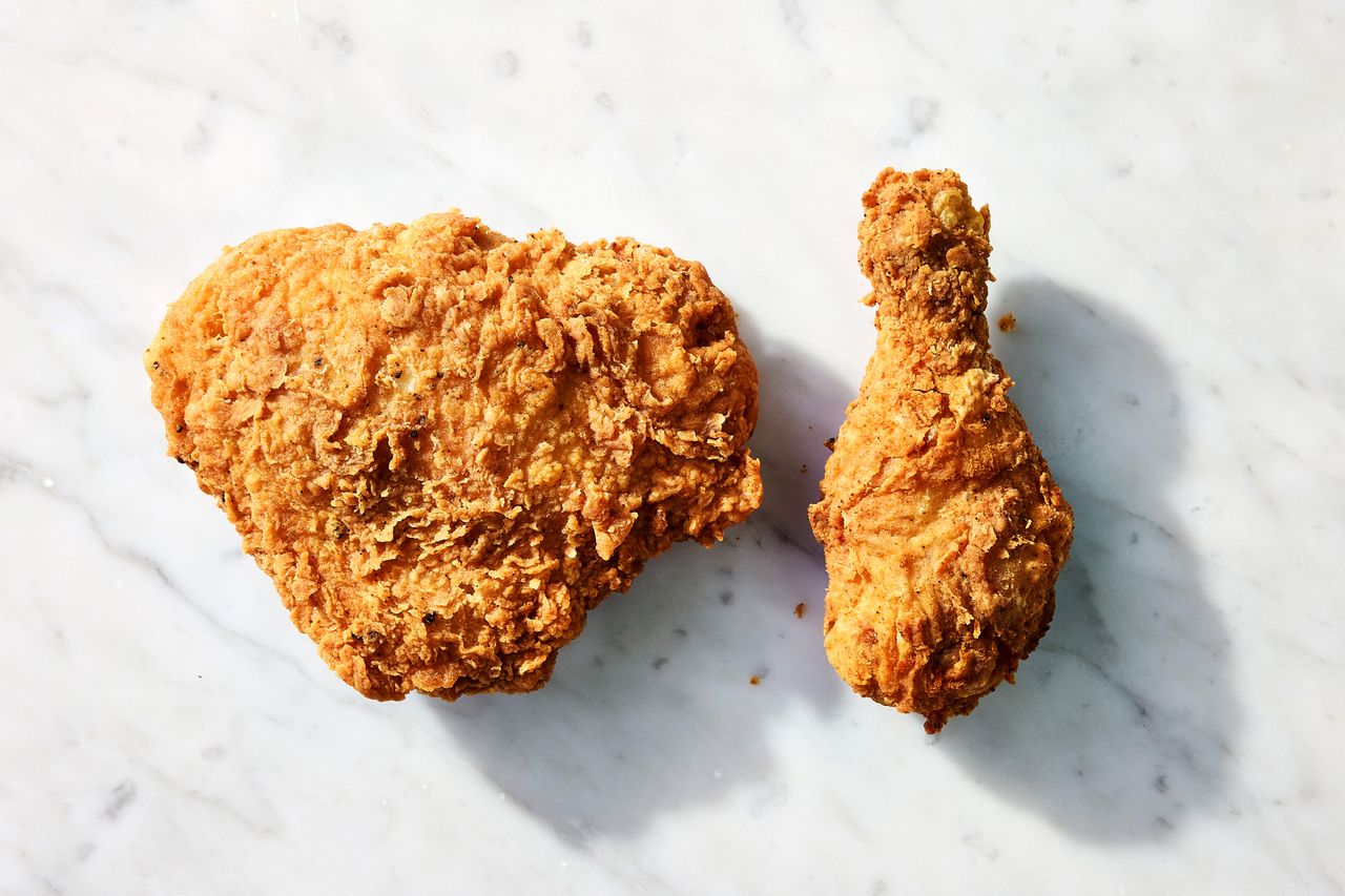 A piece of fried chicken breast and a drumstick on a marble surface