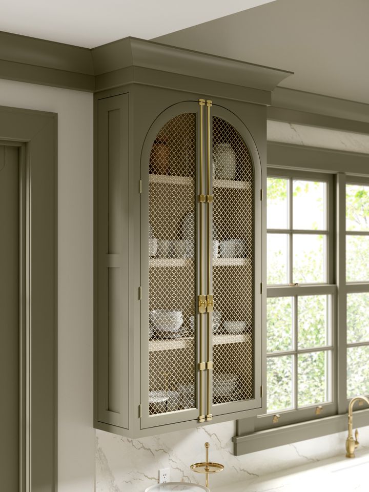 A kitchen cabinet with a mesh design and shelves displaying dishes