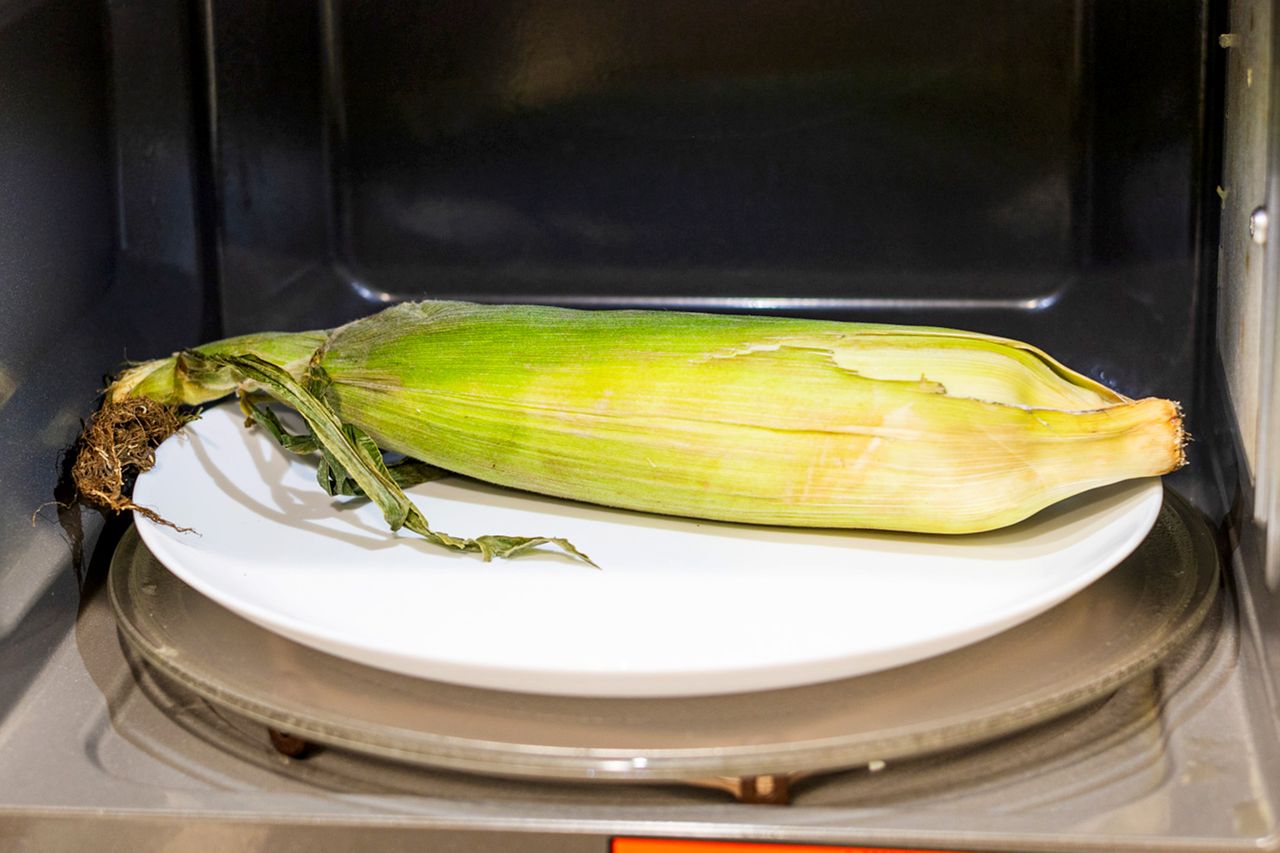 Corn on a white plate inside a microwave