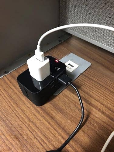 Universal power adapter with various plugged-in devices on a wooden desk