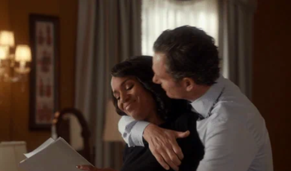 A couple shares an intimate embrace, with the woman holding papers, highlighting a moment of affection in a cozy indoor setting