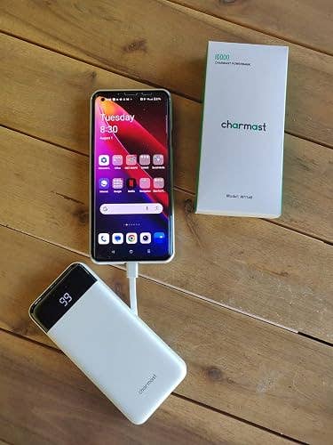 Smartphone charging with a power bank on a wooden surface; Charmast power bank packaging visible